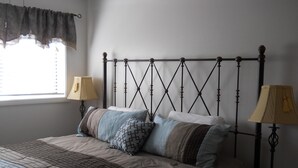 Cama bem arrumada com colcha estampada, duas luminárias de cabeceira e uma janela com cortinas.