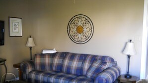 Uma sala de estar com sofá xadrez, uma mesa de centro, uma luminária e um enfeite de parede.