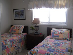 A bedroom with two beds, each with a colorful quilt, a bedside lamp, a framed picture on the wall, and a window with blinds. - Sugar Ski & Country Club Unit 535 Silver (Banner Elk)