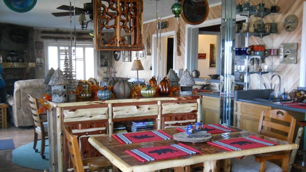 Un'area pranzo rustica con mobili in legno, una cucina sullo sfondo e diversi oggetti decorativi alle pareti.