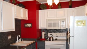 Una cucina con mobili bianchi, un fornello, un forno a microonde e un lavello.