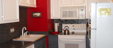 A kitchen with white cabinets, a stove, a microwave, and a sink.