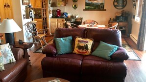 A cozy living room with a leather sofa, a wooden coffee table, and a dining area with a table and chairs.