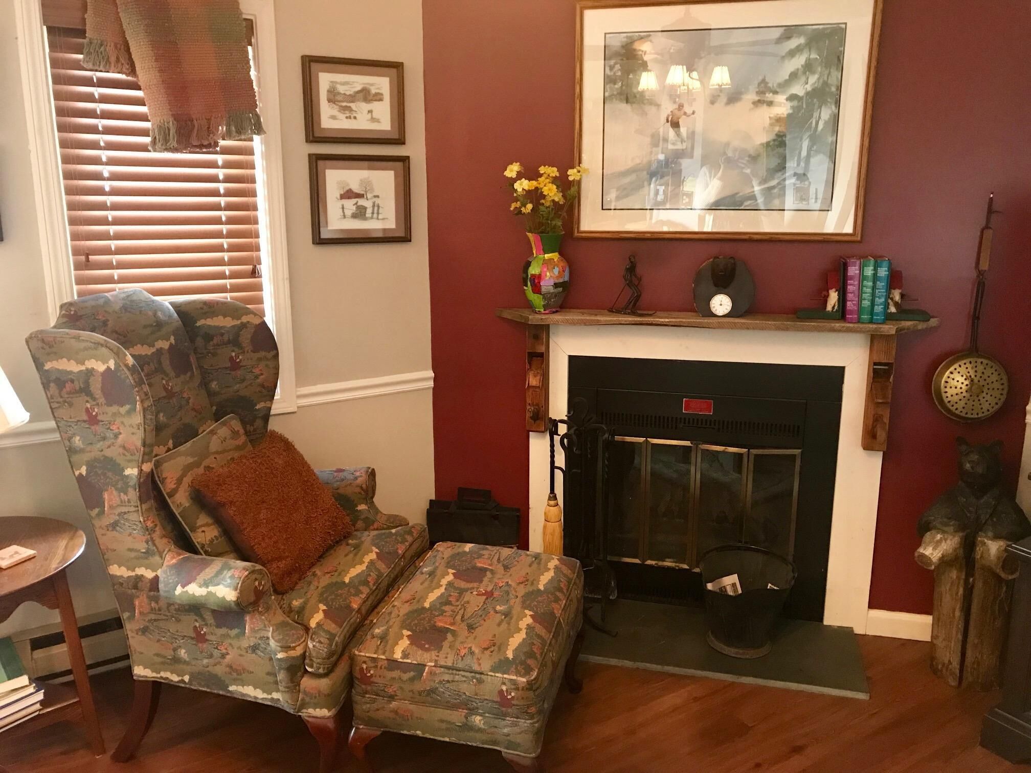 A living room with a patterned armchair, a fireplace, and framed artwork on the wall.