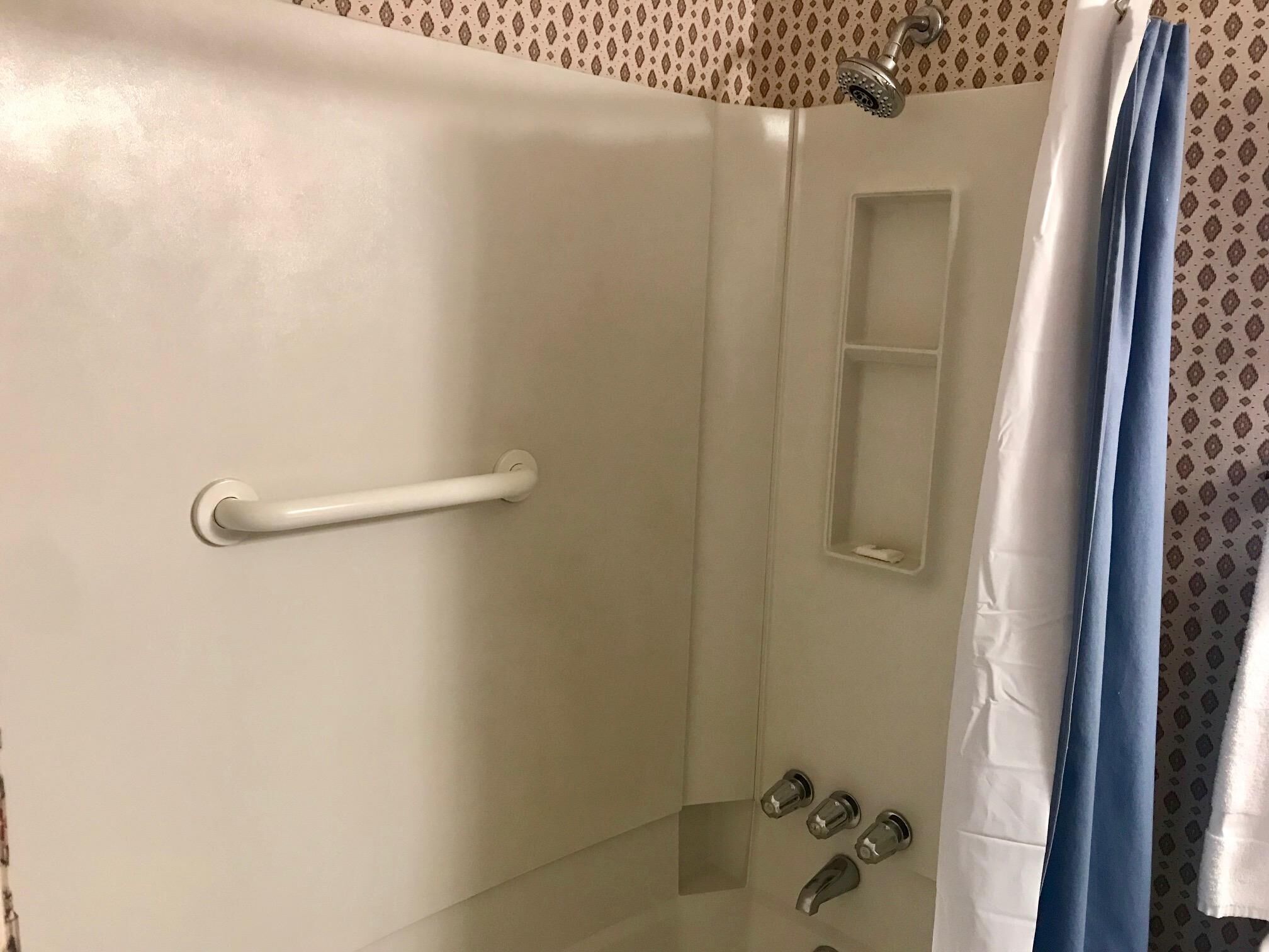 A shower with a white handle, a small shelf, and a blue curtain.