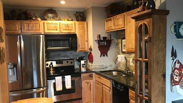 A compact kitchen with wooden cabinets, stainless steel appliances, and a built-in microwave.