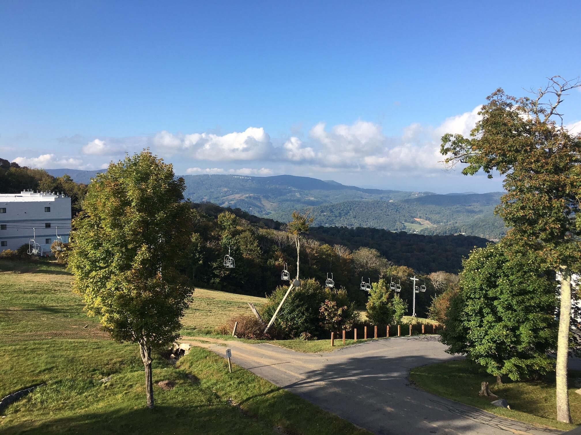 Une vue d’une route de montagne, avec un bâtiment sur la gauche et une zone boisée au loin.