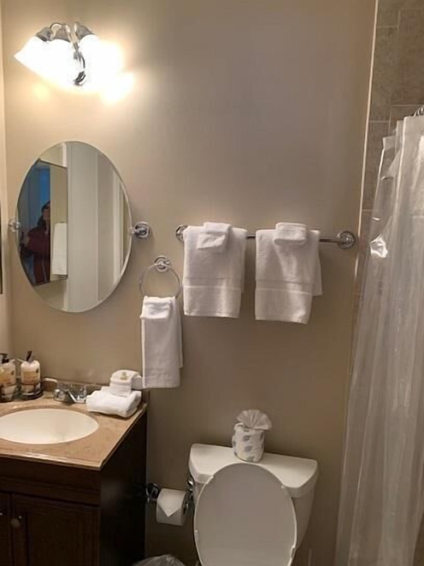 A bathroom with a round mirror, a sink, a toilet, and a towel rack with multiple towels.