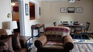 Un salon avec un canapé en cuir marron, un fauteuil à motifs, une table à manger avec des chaises et un ventilateur de plafond.