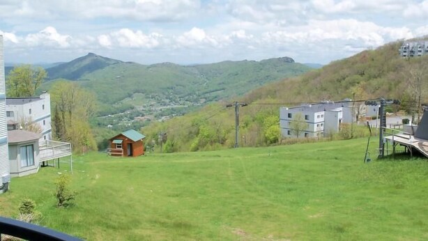 Ein Wohngebiet mit einer kleinen Holzhütte, einem modernen Haus und einer Aussicht auf grüne Hügel und ferne Berge.