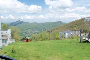 A residential area with a small cabin, a modern house, and a view of green hills and mountains in the distance.