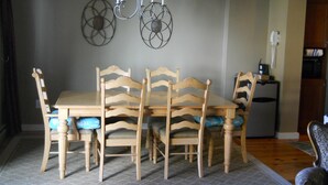 Un comedor con una mesa y sillas de madera, una araña y un adorno en la pared.