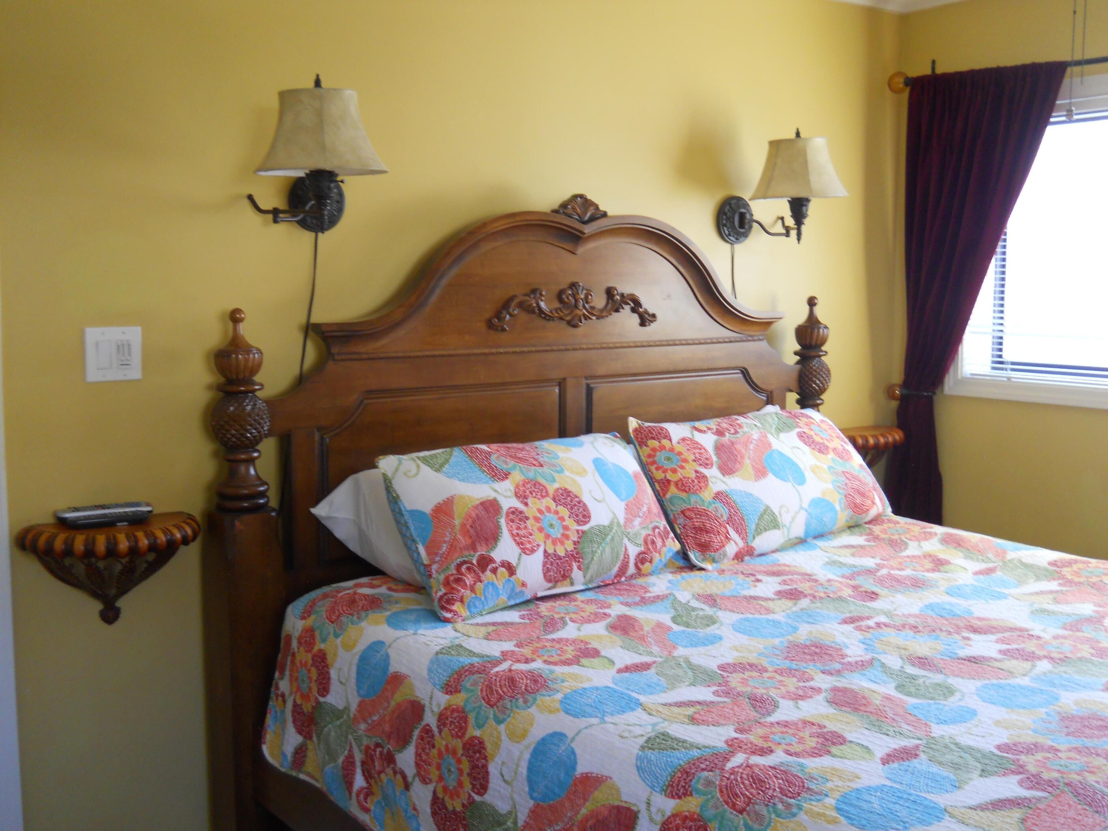 A bed with floral bedding, two wall-mounted lamps, and a wooden headboard.