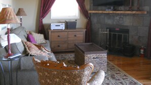 Una sala de estar con un sofá, un sillón estampado, un televisor, una chimenea y un aparador de madera.