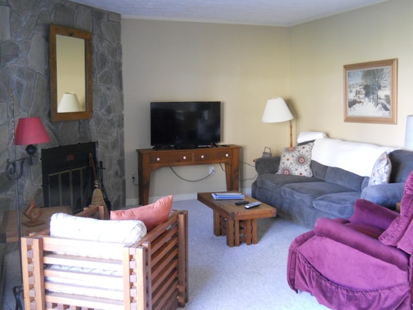 A living room with a stone wall, a fireplace, a television, a sofa, a chair, and a lamp.
