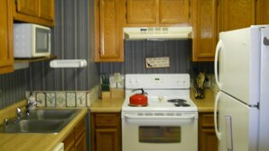 A kitchen with wooden cabinets, a white stove, a microwave, and a refrigerator.