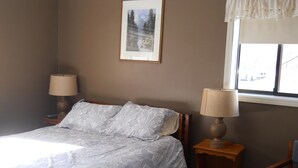 A bedroom with a bed, two bedside lamps, a chair, a window, and a framed picture on the wall.