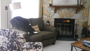 A living room with a stone fireplace, a sofa, a coffee table, and a lamp. - Sugar Ski & Country Club Unit 832 Silver (Banner Elk)
