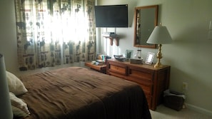 A bedroom with a bed, a dresser, a television mounted on the wall, and a mirror.