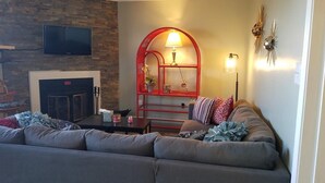 A living room with a gray sofa, a fireplace, a red arched shelf with decorative items, and a flat-screen TV mounted on a brick wall. - Sugar Ski & Country Club Unit 224 Gold (Banner Elk)