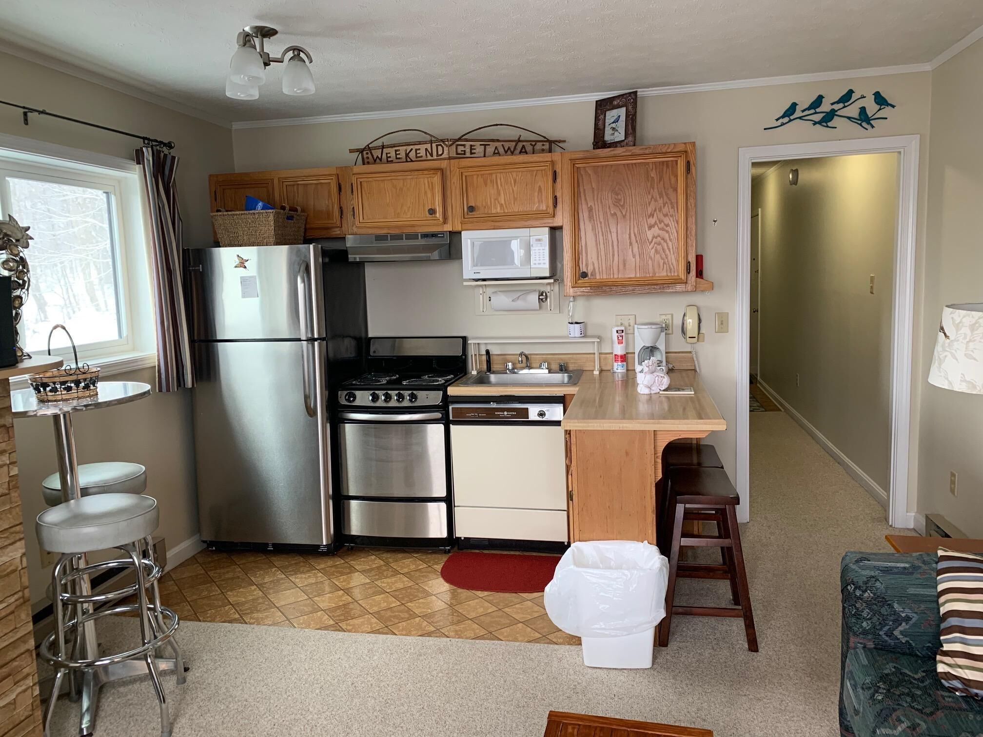 A compact kitchen with wooden cabinets, stainless steel appliances, a microwave, and a small island with stools.