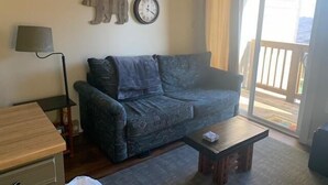 A living room with a sofa, a small table, a lamp, a clock, and a view of the outdoors. - Sugar Ski & Country Club Unit 125 Silver (Banner Elk)
