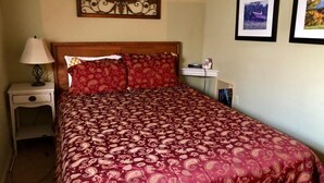 A neatly made bed with a patterned bedspread, a bedside lamp, a small shelf with a decorative item, and two framed pictures on the wall. - 10-503 (Banner Elk)