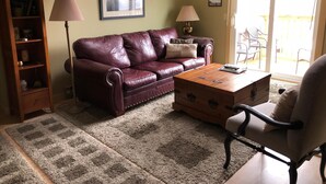 A living room with a leather sofa, a wooden coffee table, a side table, a lamp, a bookshelf, and a framed picture on the wall. - 10-503 (Banner Elk)