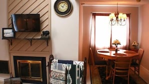 En matplats med ett runt träbord, stolar, en kristallkrona och en öppen spis.