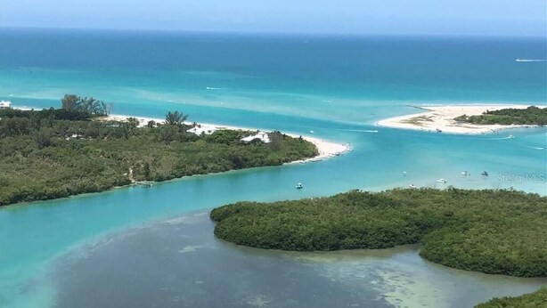 Vue aérienne d’une zone côtière avec des eaux turquoise limpides, plusieurs petites îles et une plage de sable.