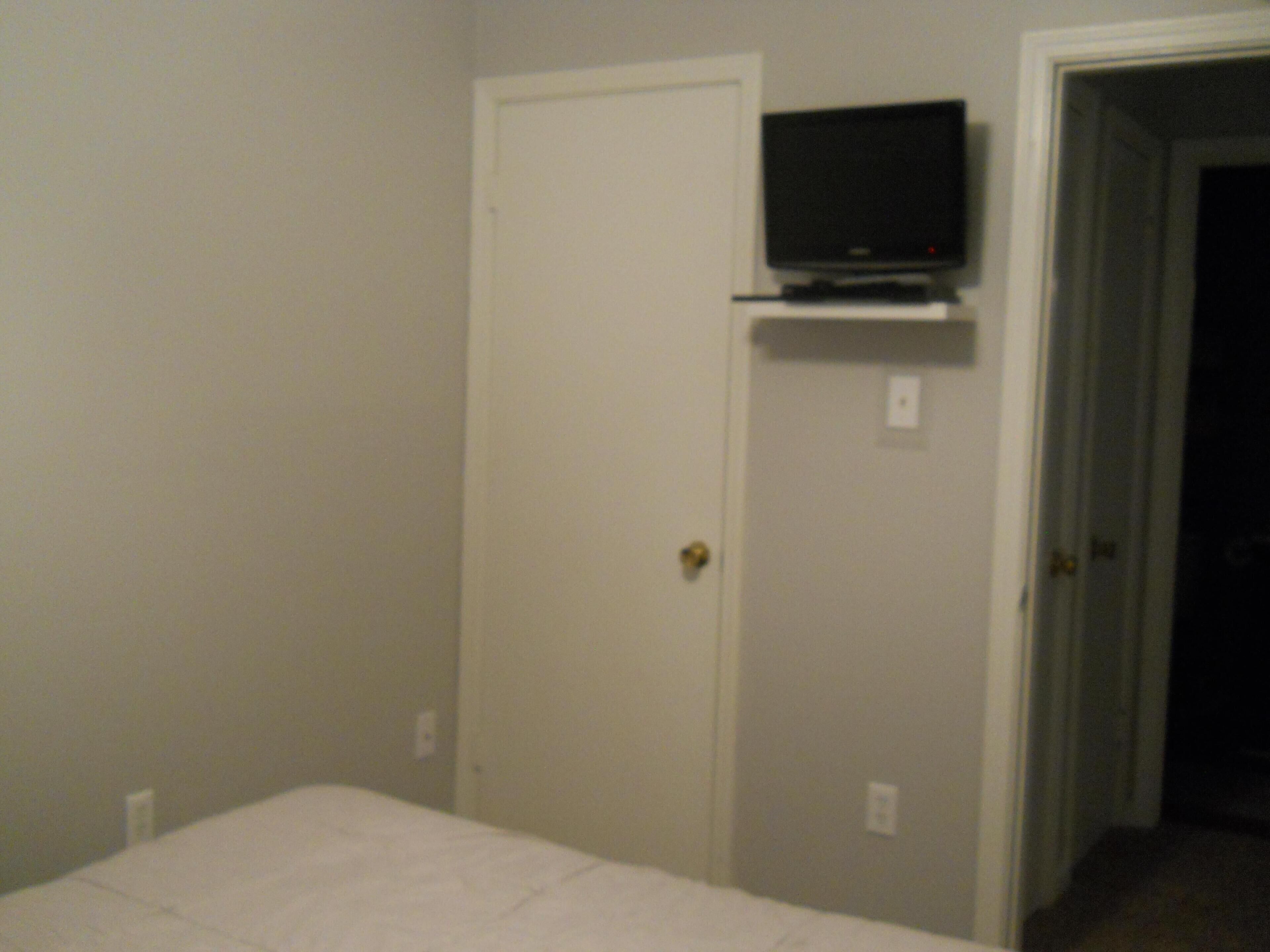 A room with a bed, a television mounted on a wall, and a door leading to another room.