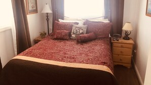 Ein ordentlich bezogenes Bett mit einem gemusterten Überwurf, ein Nachttisch mit Lampe und eine kleine Pflanze.