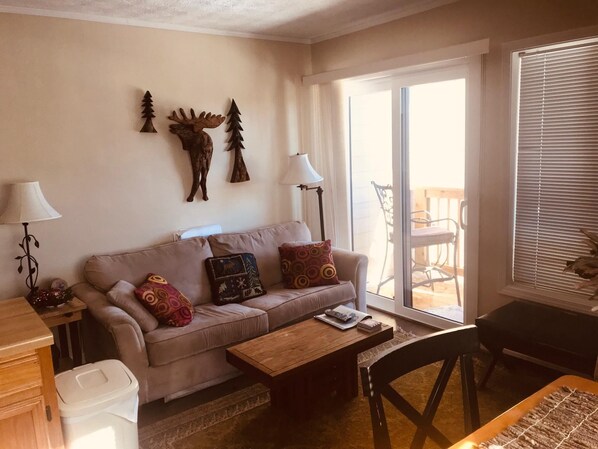 Una sala de estar con sofá, una mesa de centro, una lámpara y un ventanal corredizo que da a un espacio exterior.