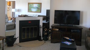 Un salon avec une cheminée, un téléviseur et un ventilateur de plafond.