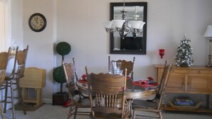 Un coin repas avec une table ronde, des chaises en bois, un lustre, une horloge et un petit sapin de Noël.