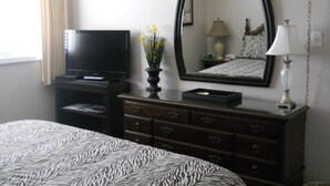 Une chambre d’hôtel avec un lit, une commode, une télévision, un miroir et une lampe.