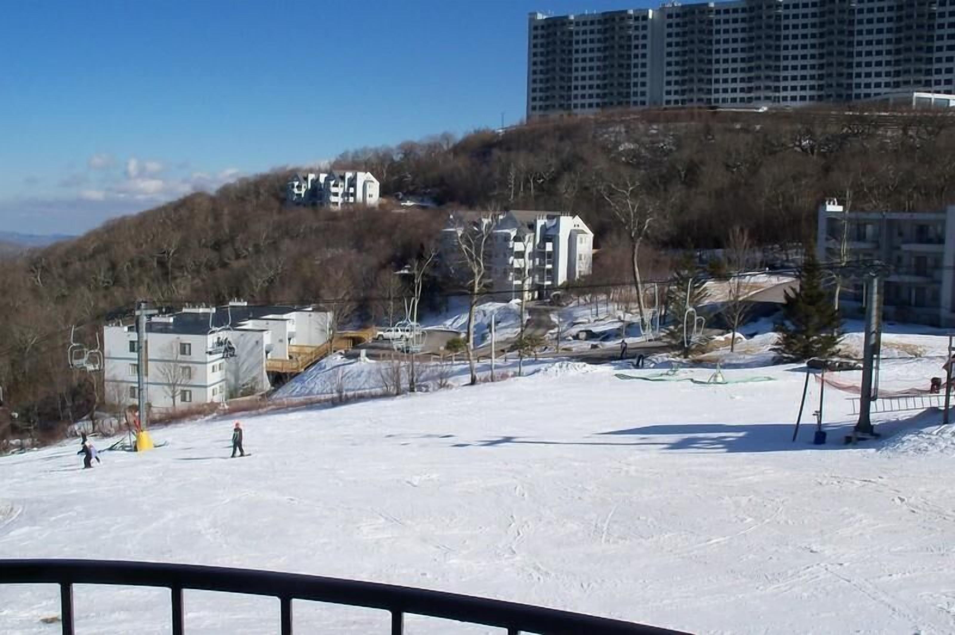 A snowy ski slope with buildings in the background.