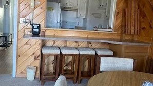 Kompakti keittiö, jossa on puupanelointi, suuri peili ja baaritiski jakkaroineen.
