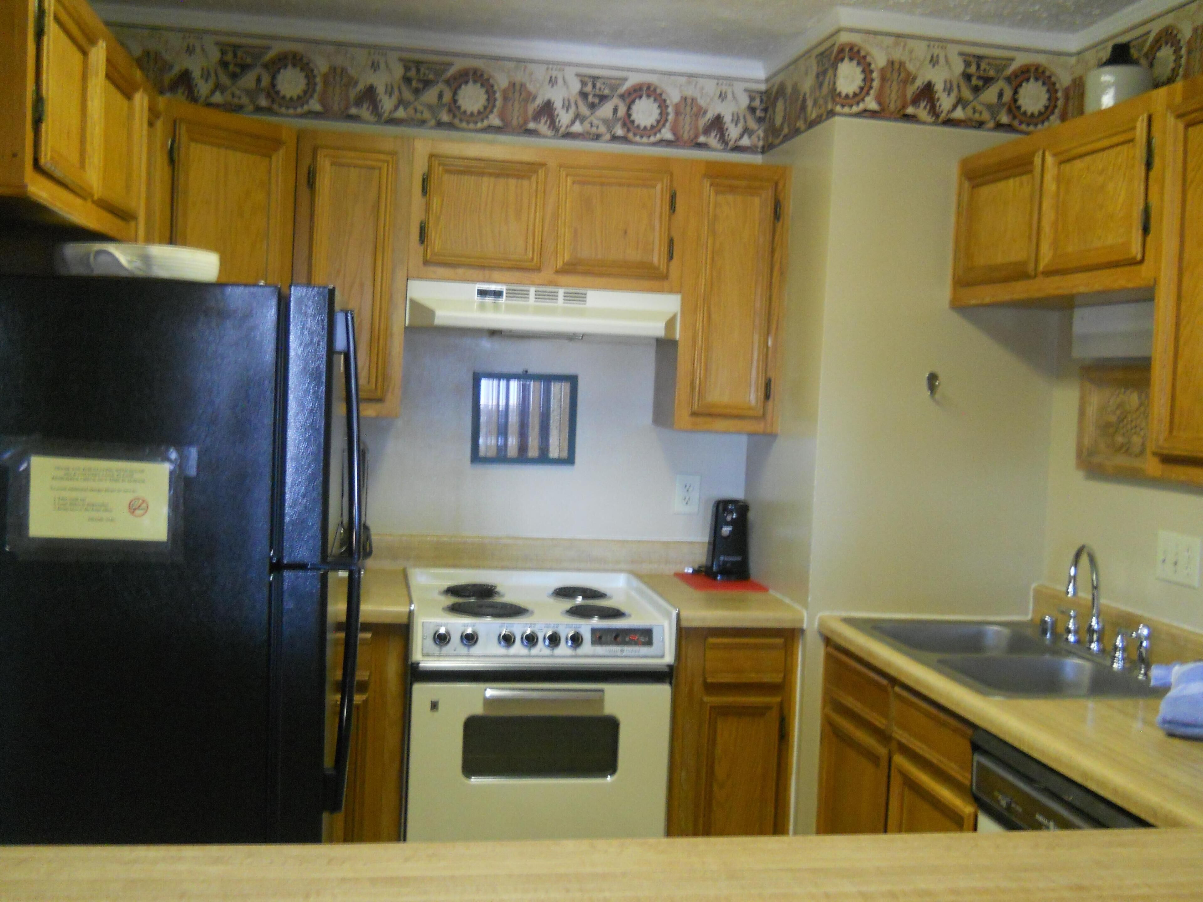 A kitchen with wooden cabinets, a black refrigerator, a stove, and a sink.