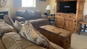 Ein Wohnzimmer mit einer Holz-Unterhaltungsecke, einer Couch mit gemusterten Kissen, einem Fernseher und einem Kamin.