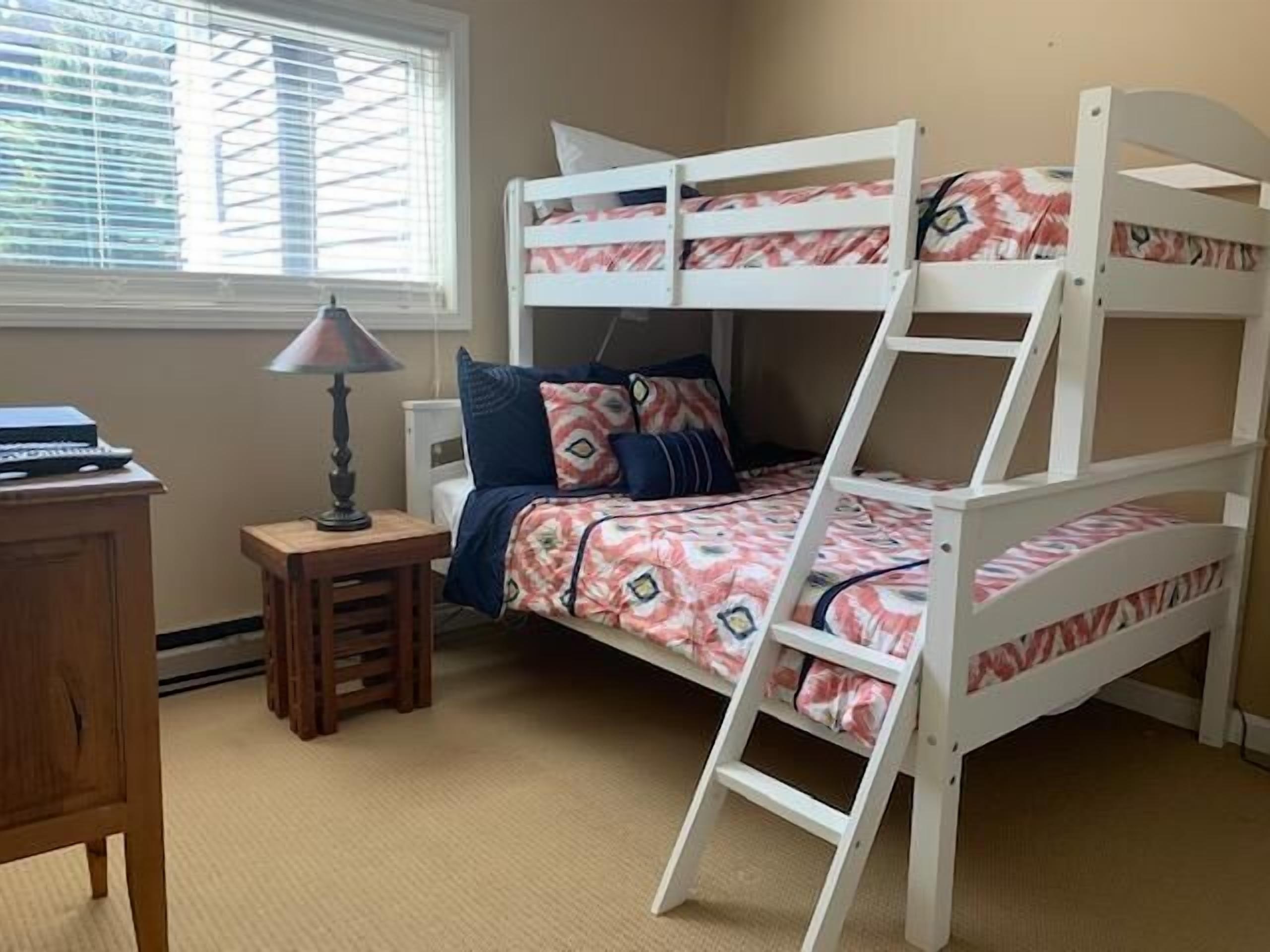 A bunk bed room with a desk, lamp, and window.
