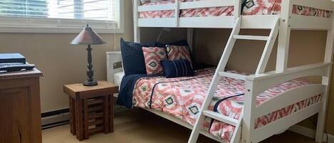 A bunk bed room with a desk, lamp, and window.