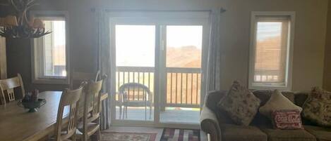 A living room with a dining area, a sofa with cushions, a coffee table, and a view of the desert through the sliding doors.