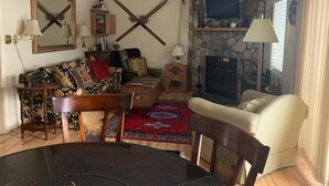 A cozy living room with a fireplace, a stone wall, a television, and a dining area with a table and chairs. - Sugar Ski & Country Club Unit 433 Gold (Banner Elk)