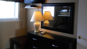 A room with a TV mounted on the wall, two bedside lamps, a mirror, and a small dresser with drawers. - Sugar Ski & Country Club Unit 511 Gold (Banner Elk)