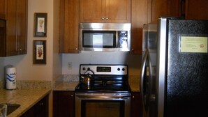 Une cuisine avec des meubles de rangement en bois, un four à micro-ondes en acier inoxydable, un réfrigérateur noir et une cuisinière.