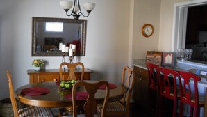 Un coin repas comprenant une table en bois, des chaises, un lustre, un miroir et une horloge murale.