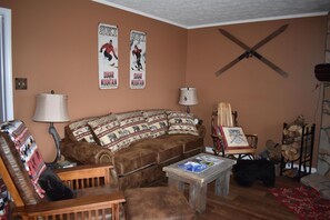 A cozy living room with a brown sofa, patterned cushions, a wooden coffee table, and a fireplace with a log rack.