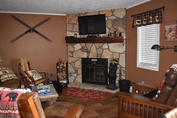 A cozy living room with a stone fireplace, a mounted TV, and a bear statue.
