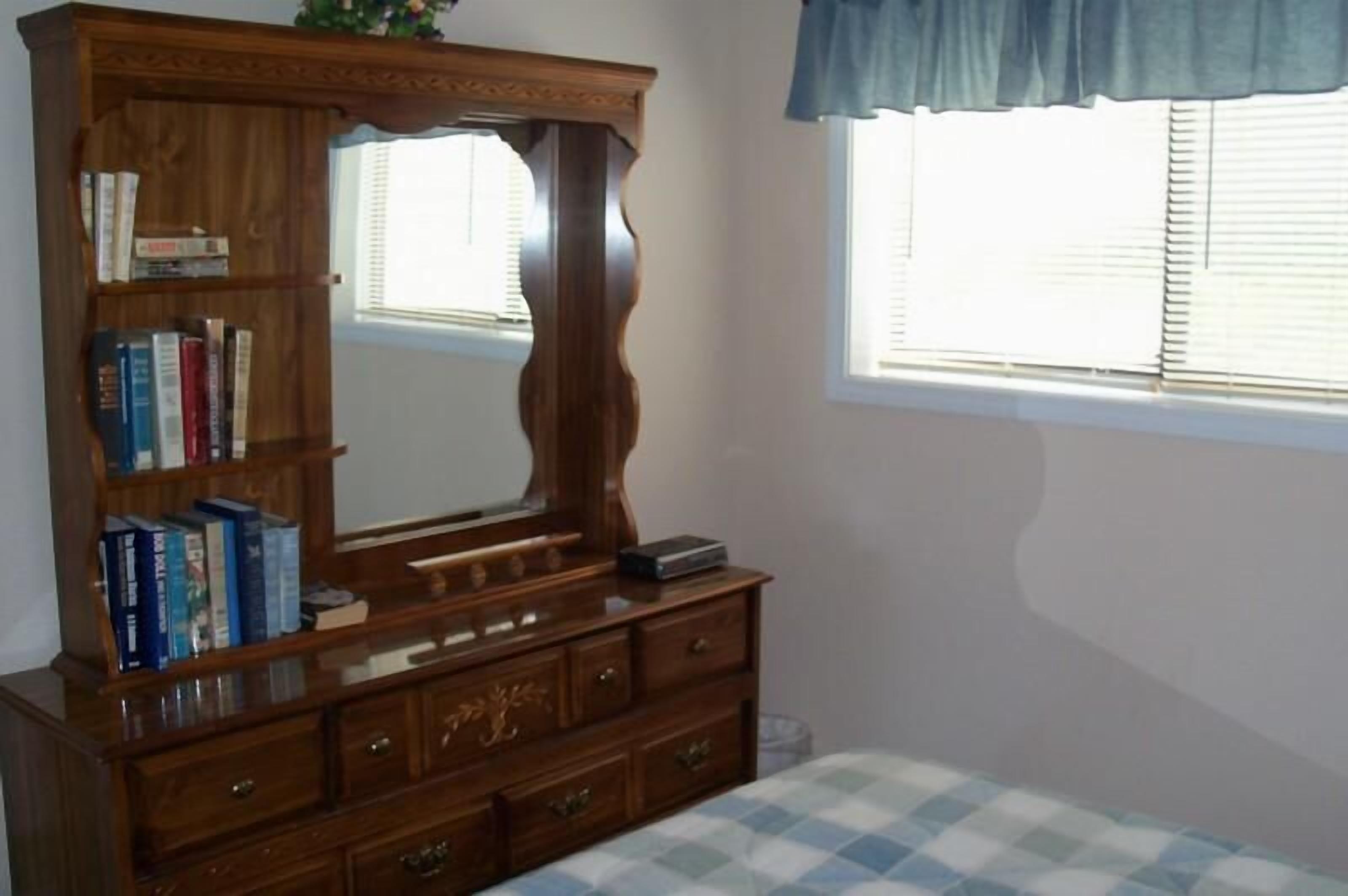 A wooden dresser with a mirror, books, and drawers.